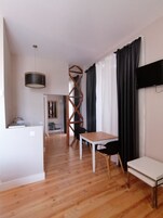 Una sala moderna con piso de madera, una mesa blanca, una silla negra, un televisor montado en la pared y una estructura de madera en espiral única.