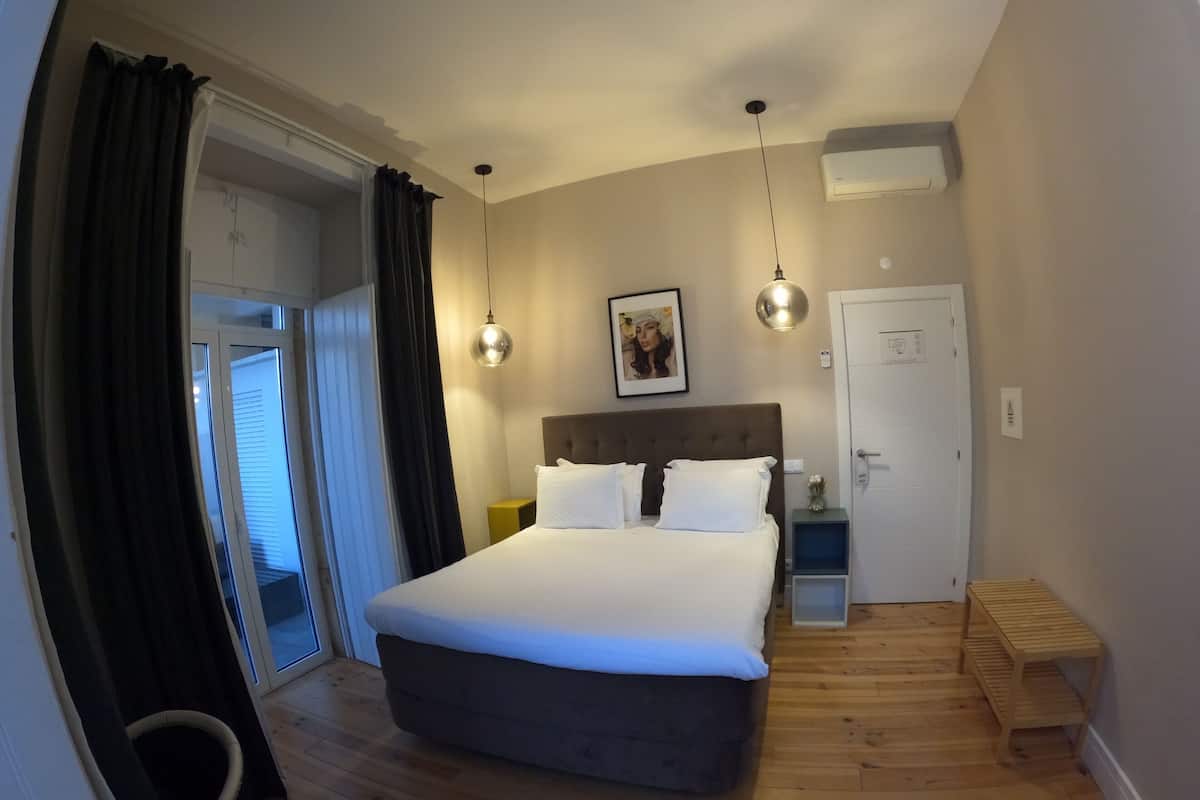 A hotel room with a large bed, a bedside table, a nightstand, a wall-mounted air conditioner, and a door.