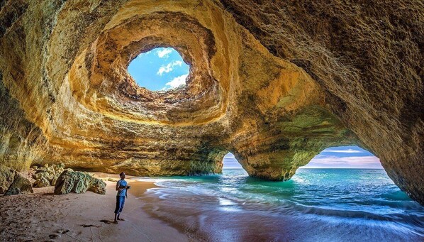 Une formation rocheuse naturelle dotée d’une ouverture circulaire, une plage de sable et l’océan.