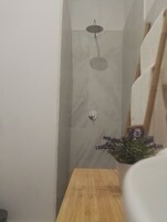 A bathroom with a shower, a wooden bench, and a potted plant with purple flowers.