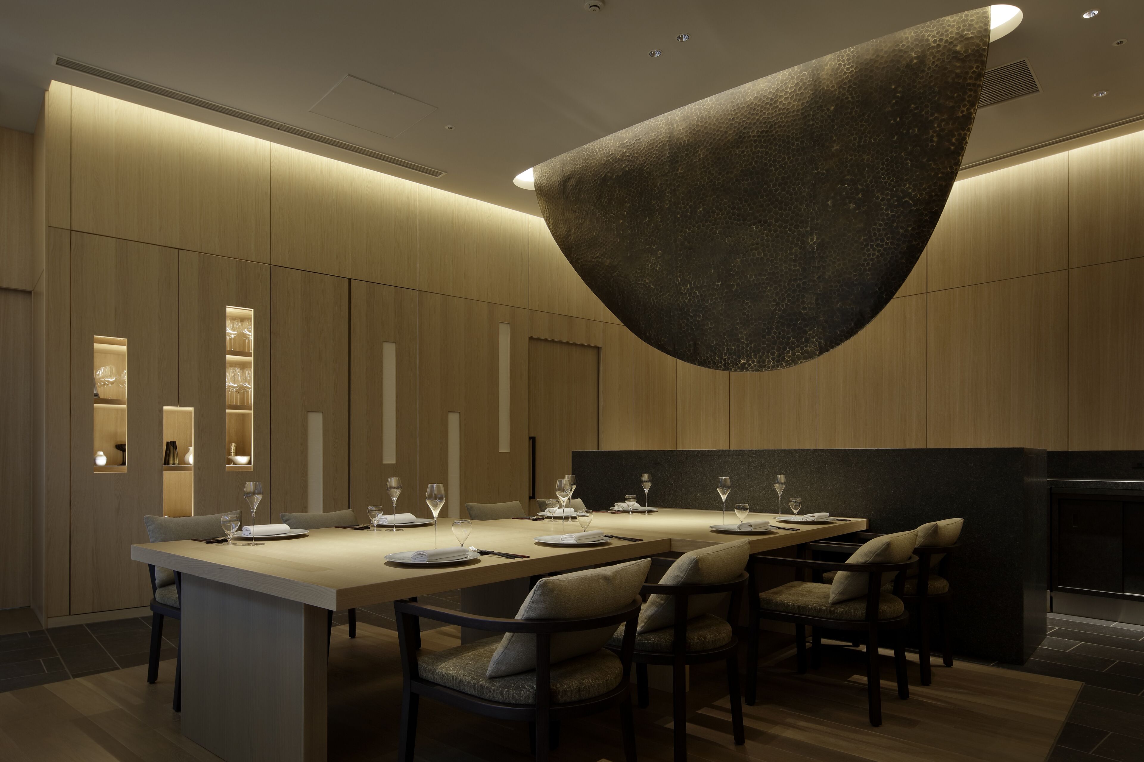 A modern dining area with a long table, multiple chairs, and a unique hanging light fixture.
