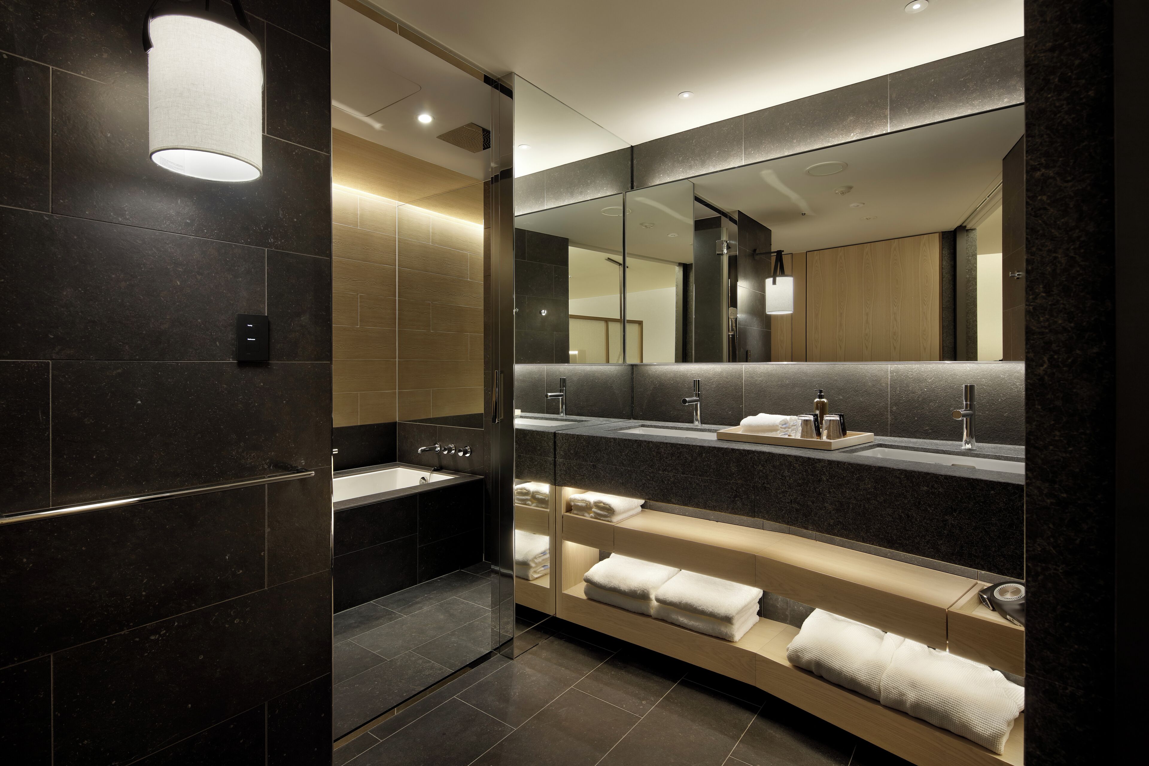 A modern bathroom with a large mirror, a bathtub, and a vanity with a sink and towel rack.