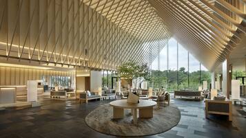 A spacious lobby with a high ceiling, modern furniture, and large windows offering a view of the outdoors.