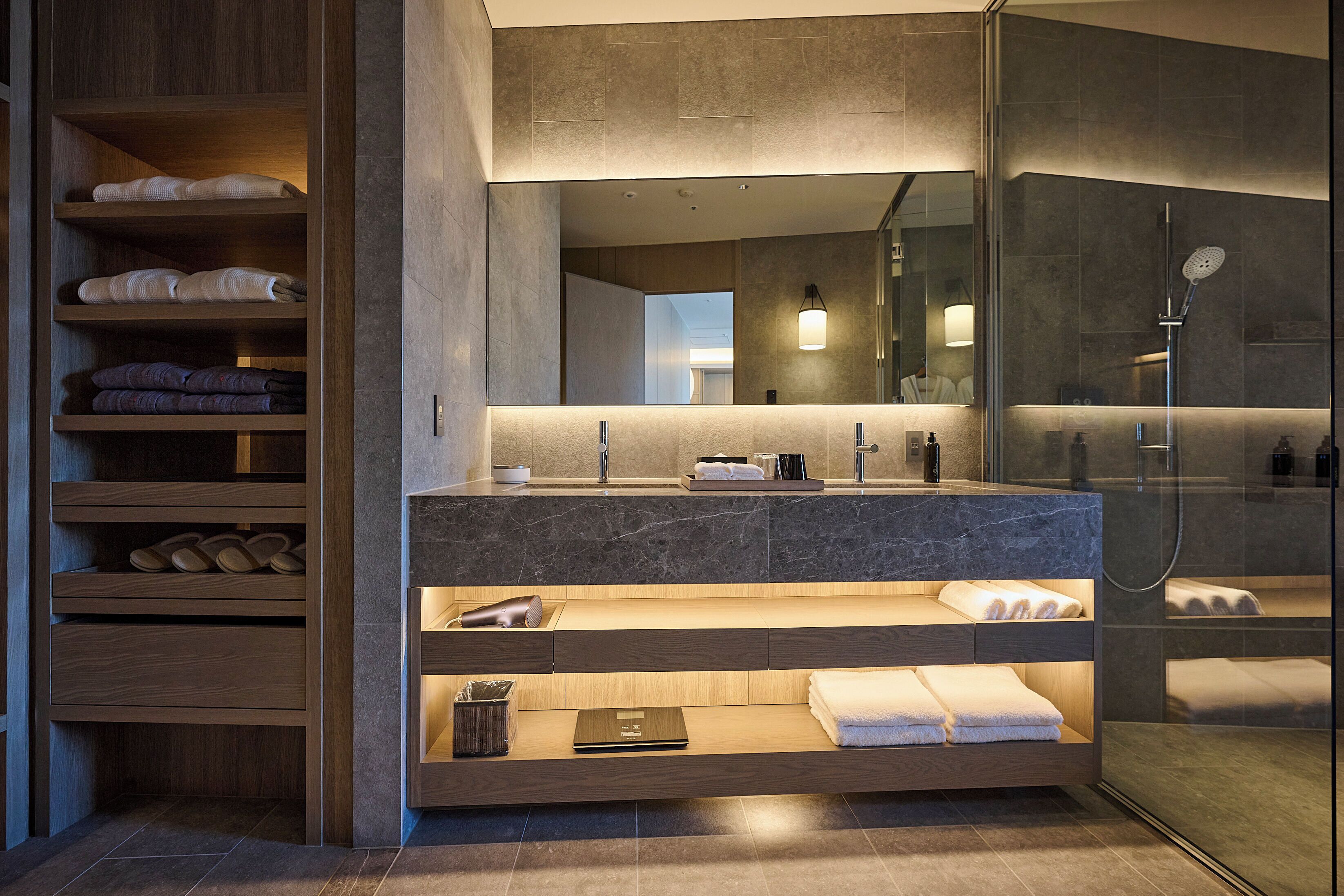 A modern bathroom with a marble sink, built-in shelves, a glass shower enclosure, and a large mirror.