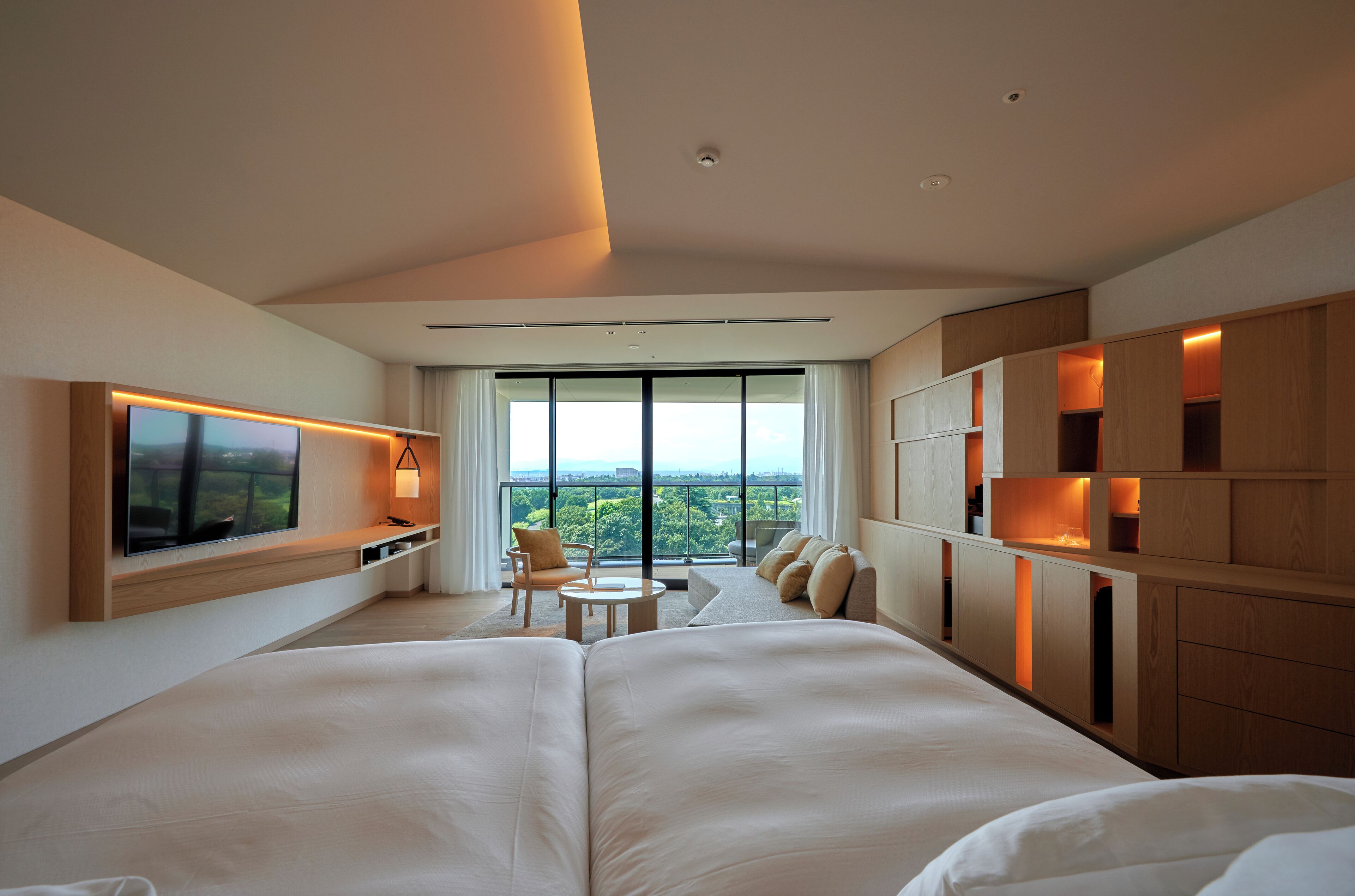 A modern hotel room with a large bed, a TV, a seating area with a view, and built-in wooden storage.