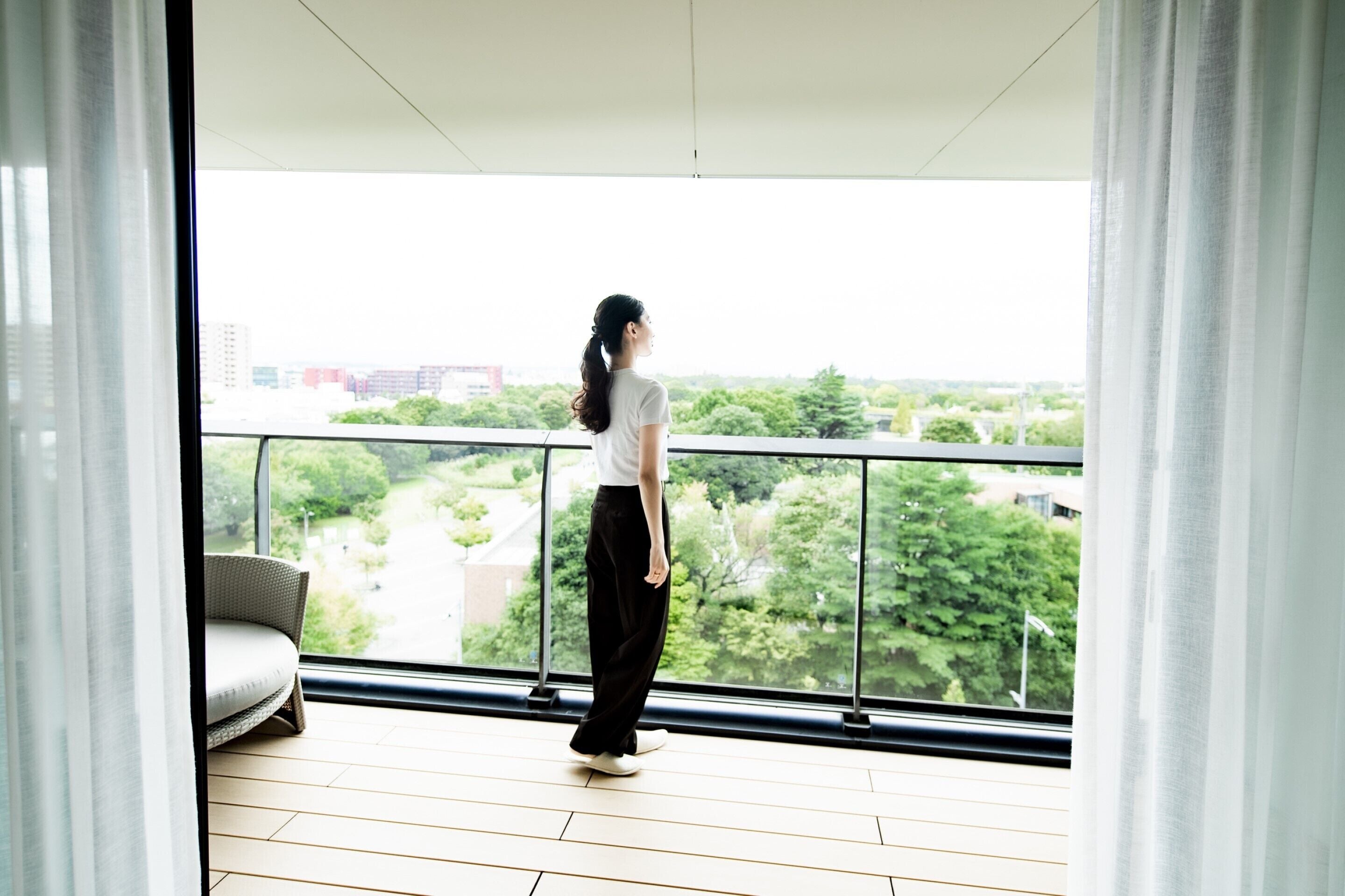 A person standing on a balcony with a view of a cityscape and greenery.
