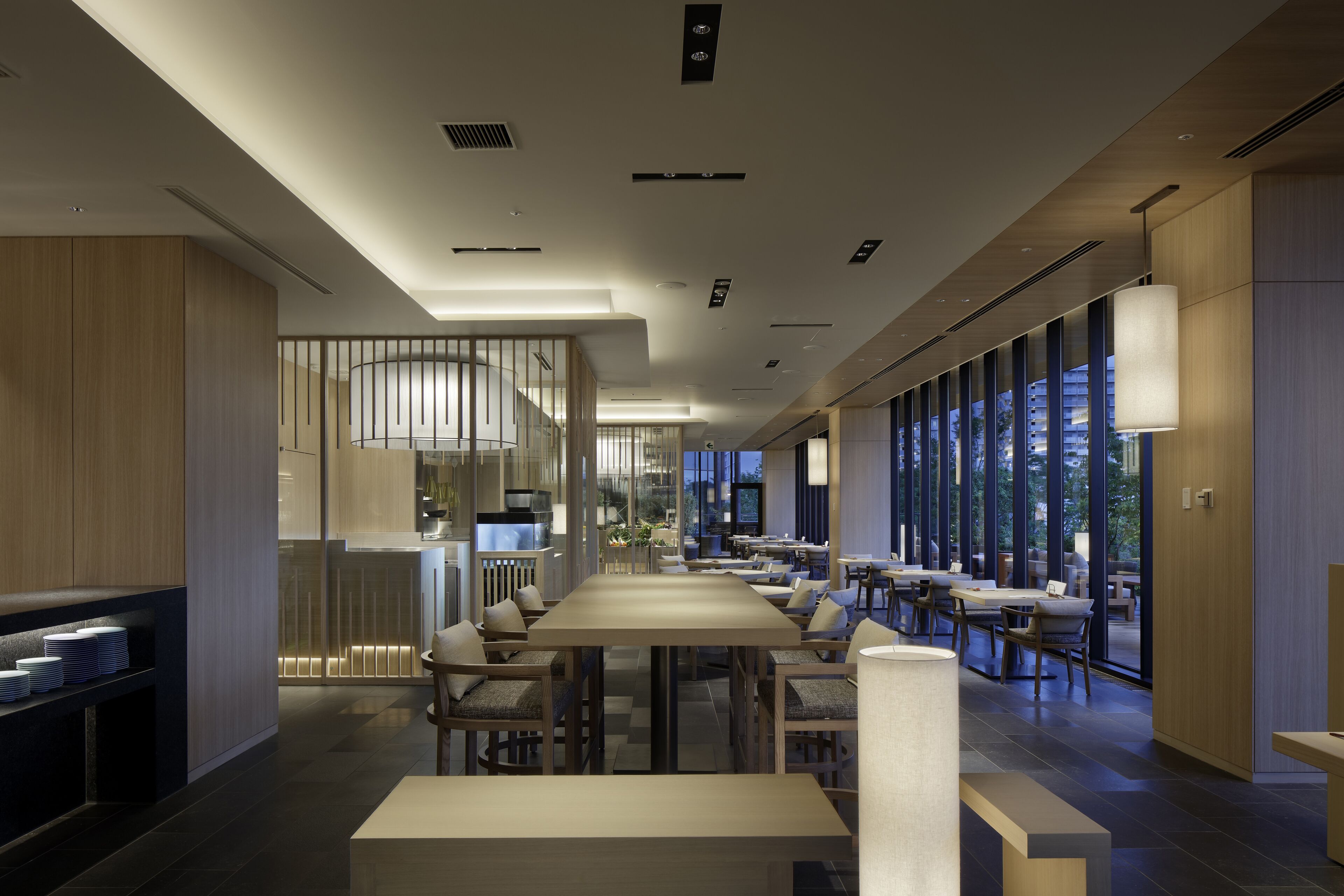 Un restaurante moderno con una larga mesa de comedor, numerosas sillas y vistas a la ciudad a través de grandes ventanales.