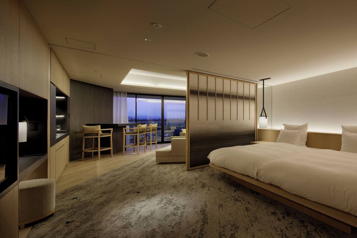 A modern hotel room with a large bed, a TV, a desk, and a view of the city.