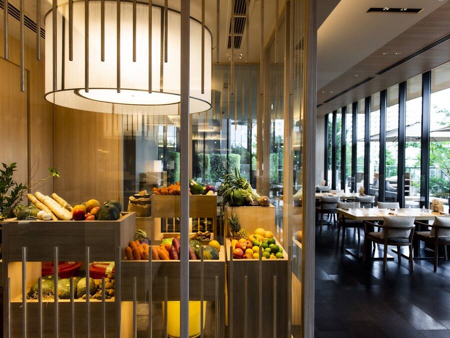 A modern dining area with wooden furniture and a variety of fruits and vegetables displayed in wooden crates.