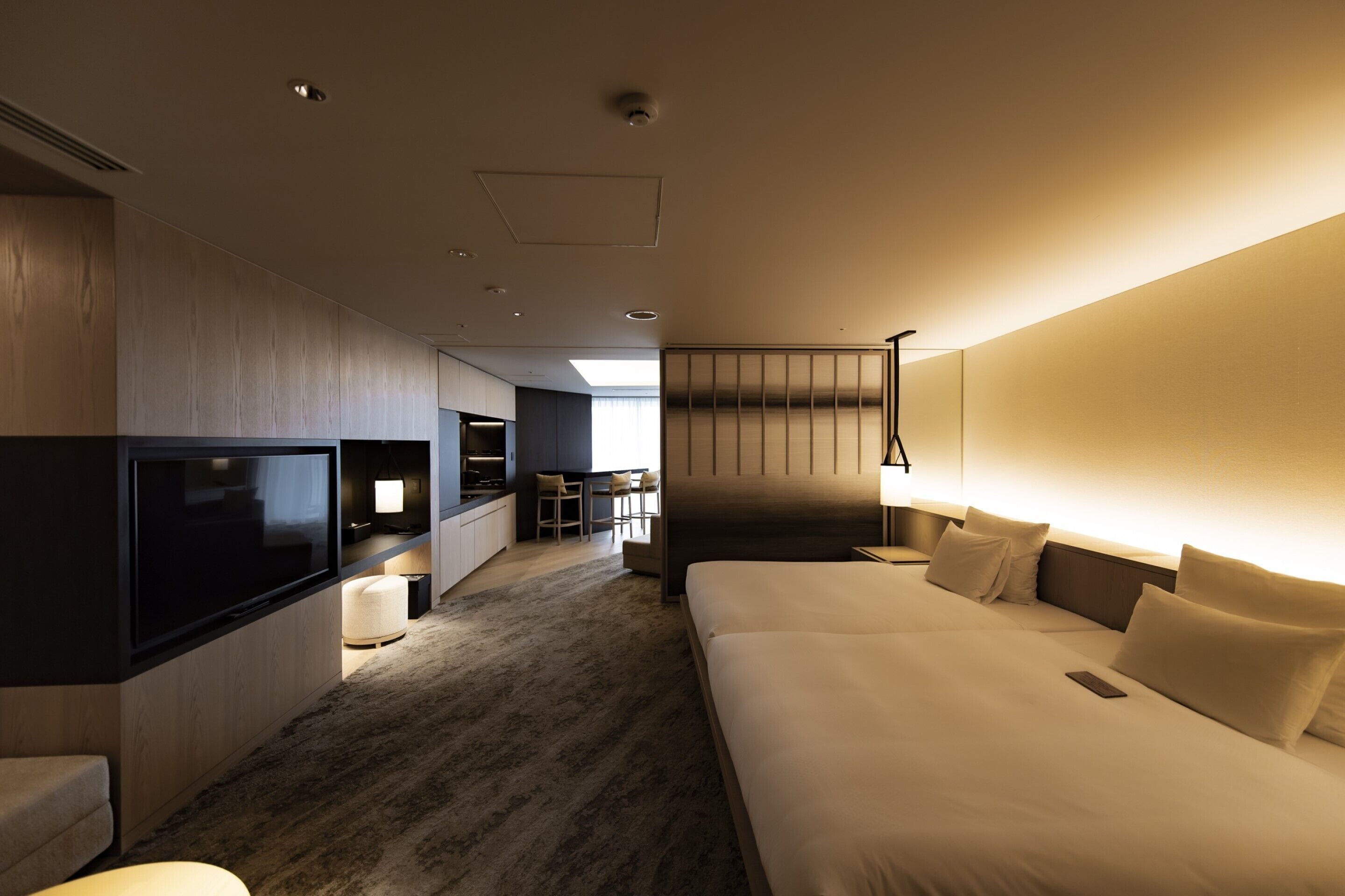 Ein modernes Hotelzimmer mit einem großen Bett, einem Flachbildfernseher, einem Schreibtisch mit Stuhl und einer kleinen Küchenzeile.