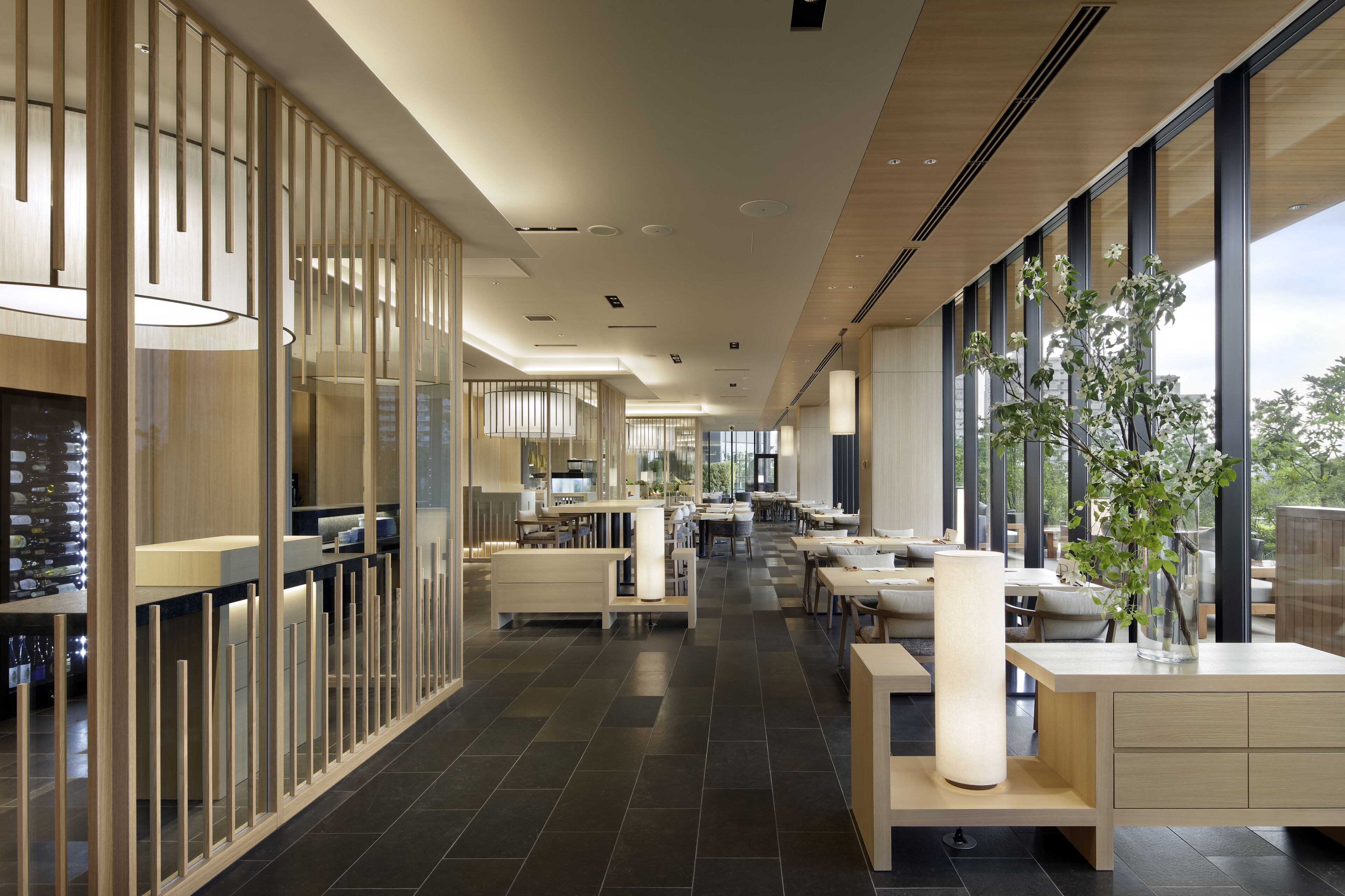 A modern hotel lobby with a long reception desk, seating areas, and large windows offering views of the outdoors.
