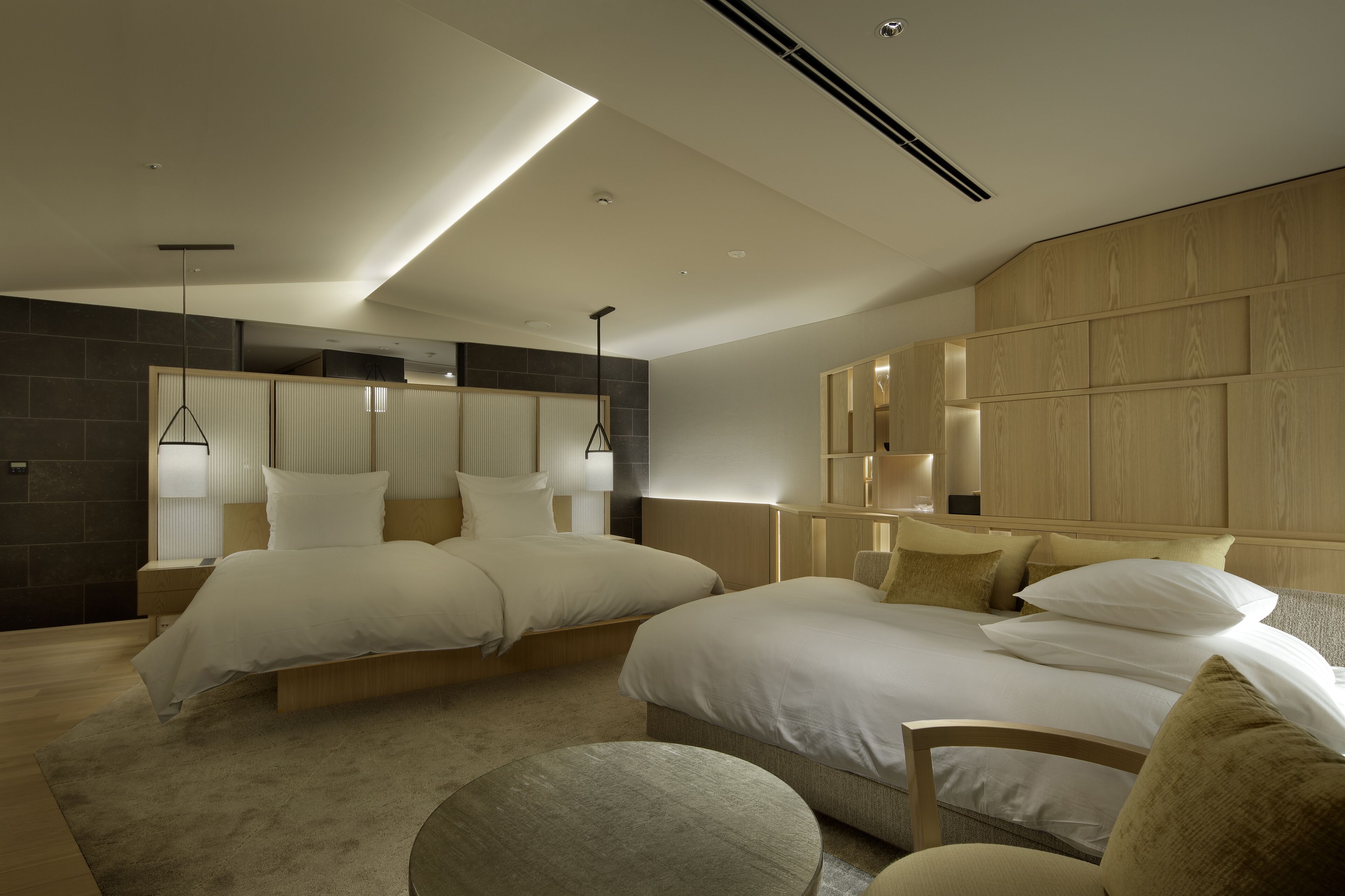 A modern hotel room with two beds, a sitting area, and a large window.
