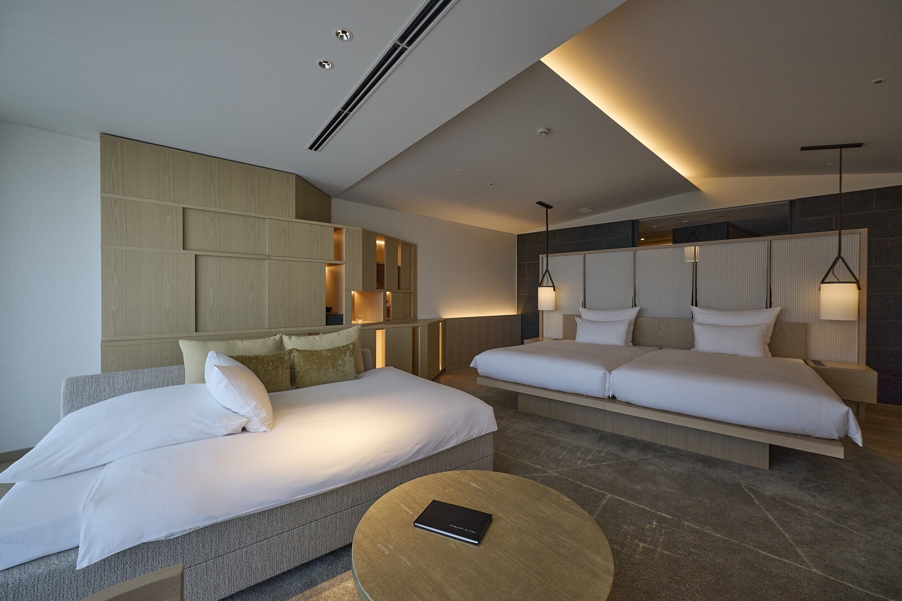 A modern hotel room with two beds, a round coffee table, and a large mirror.
