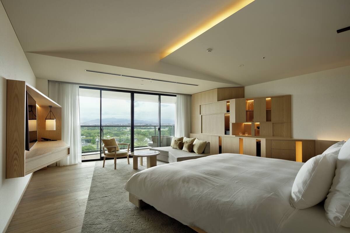 A modern hotel room with a large bed, a seating area with a view, and built-in storage.
