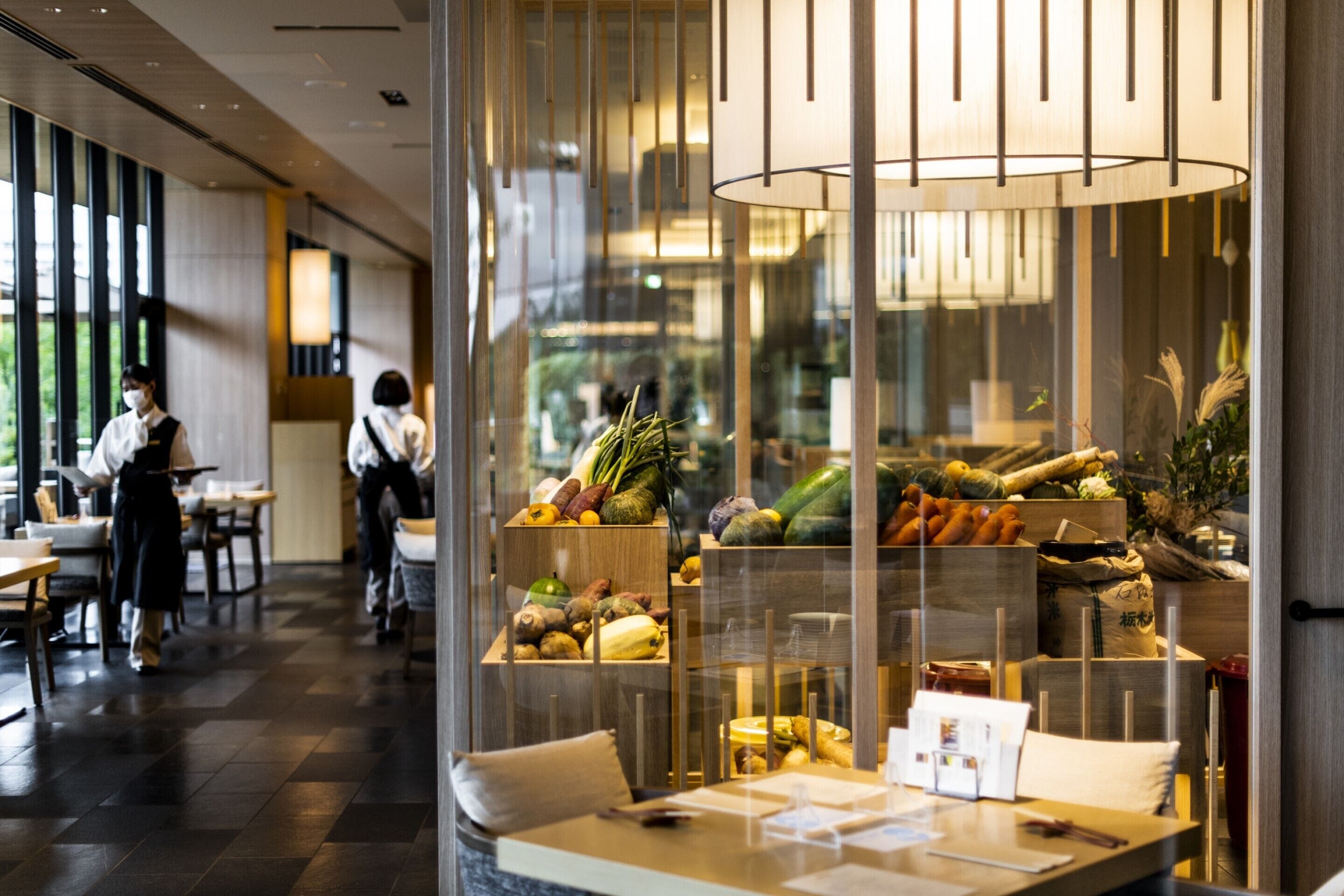 A restaurant with a modern interior, featuring a central display of fresh produce and a seating area with tables and chairs.