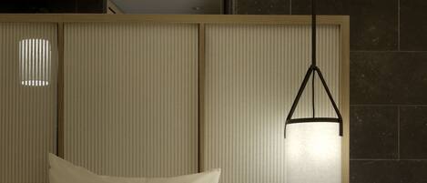 A modern hotel room with a bed, a bedside table, a hanging light fixture, and a textured wall panel.