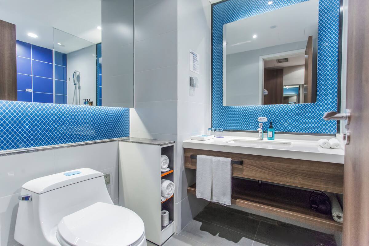 Un baño moderno con inodoro blanco, lavamanos con espejo y zona de ducha.