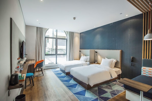 A modern hotel room with two beds, a desk, a chair, and a large window.
