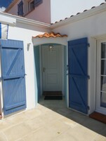 Entrada de un edificio con dos puertas azules, una puerta blanca y suelo de baldosas.