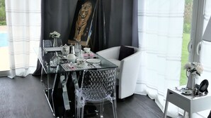 A modern room with a glass dining table, clear chairs, a white sofa, and a painting of a tiger on the wall. - Chambre d'hôte Blanche Pierre B&B (Le Perrier)