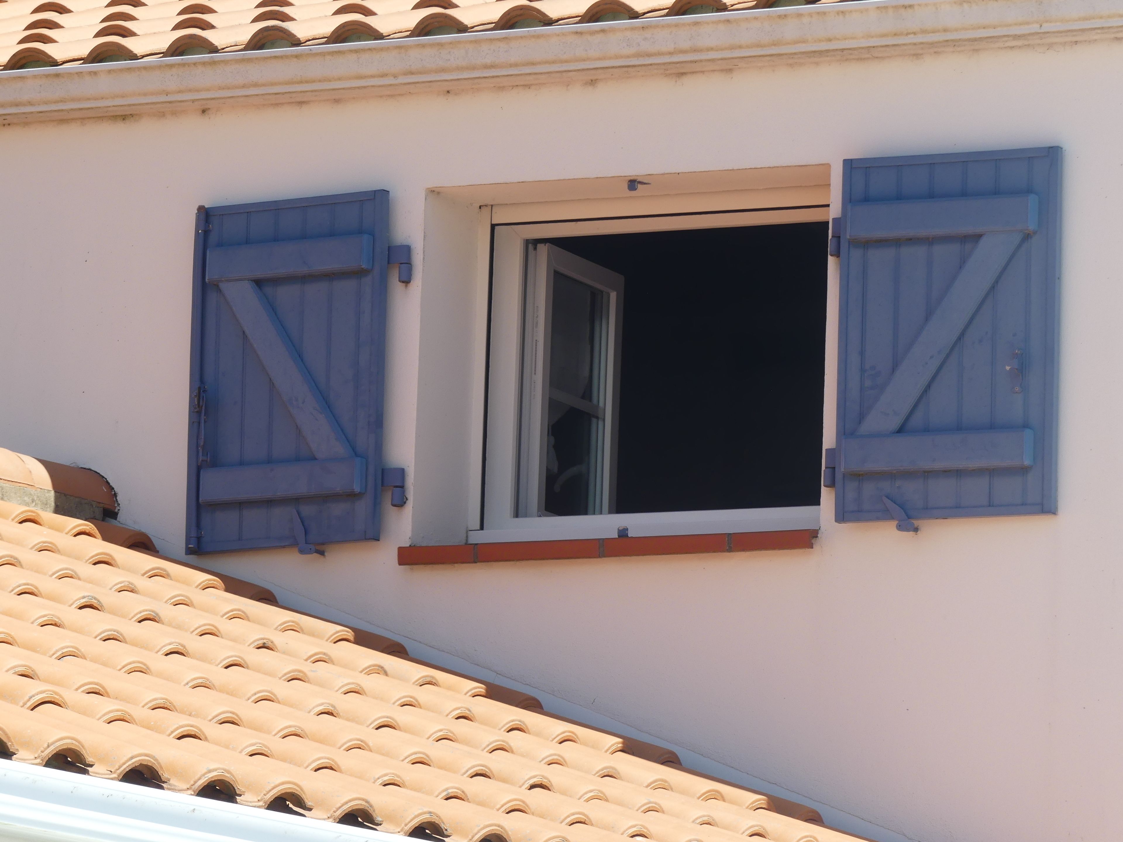 Un bâtiment doté d’une fenêtre et de volets, d’un toit en tuiles et d’un petit balcon.