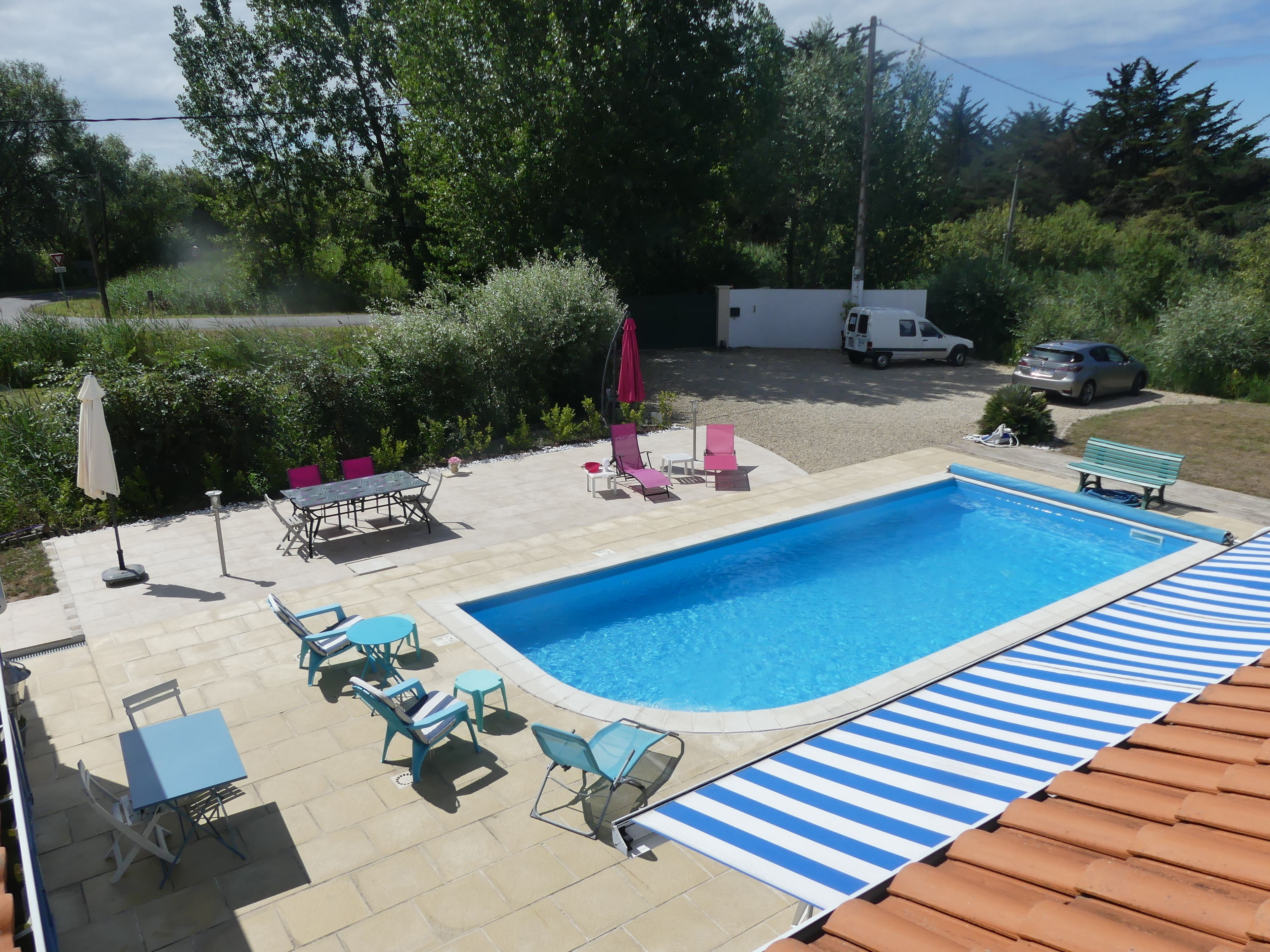 Une piscine rectangulaire aux parois bleues, entourée d’un patio aménagé avec des meubles d’extérieur et une terrasse carrelée.