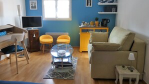 A living room with a sofa, a small table, a TV, a radiator, and a window. - Chambre d'hôte Blanche Pierre B&B (Le Perrier)