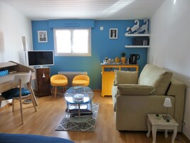 Una sala de estar con sofá, una mesita, televisor, radiador y ventana.