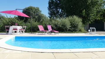 A swimming pool with a tiled deck, surrounded by lounge chairs and a table with chairs.