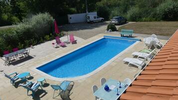 Ein rechteckiger Swimmingpool mit einer gefliesten Sonnenterrasse, umgeben von Liegestühlen und Tischen.