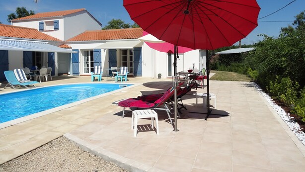 A poolside area with lounge chairs, a red umbrella, and a house with a tiled roof. - Chambre d'hôte Blanche Pierre B&B (Le Perrier)