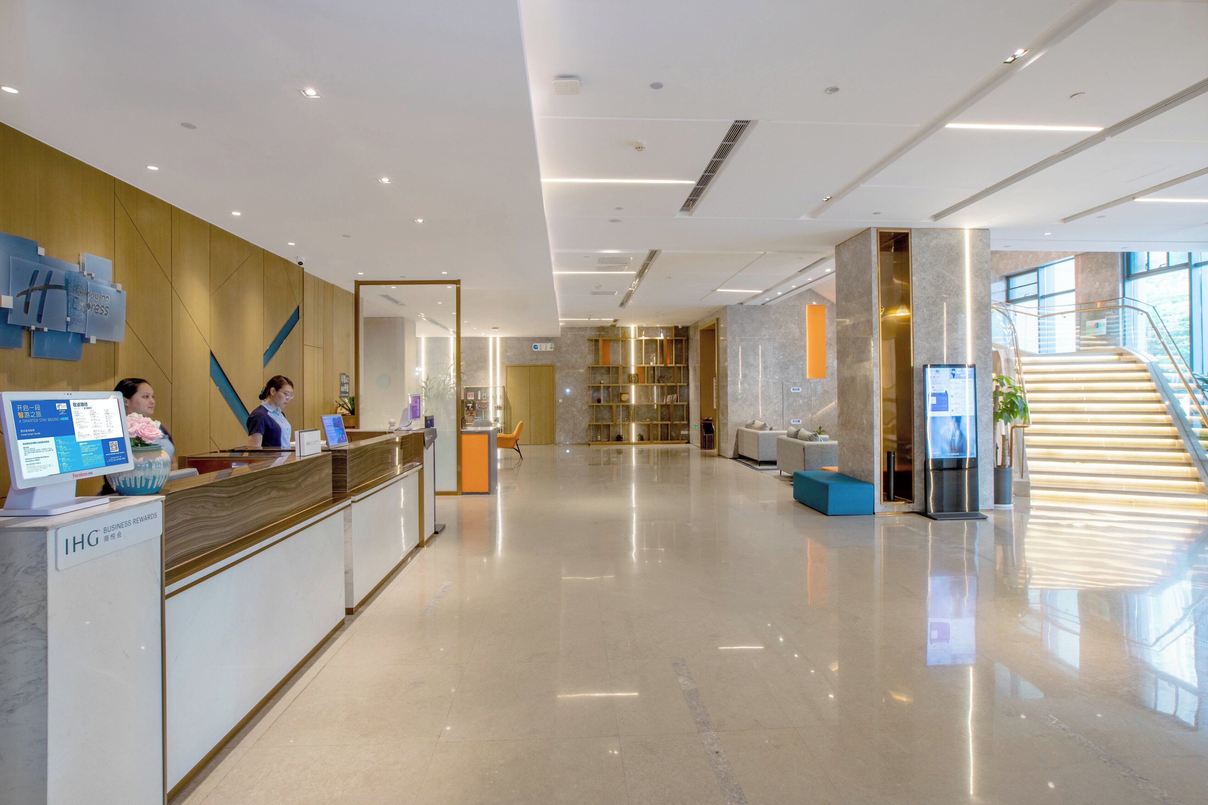 A modern hotel lobby with a reception desk, a staircase, and a seating area.