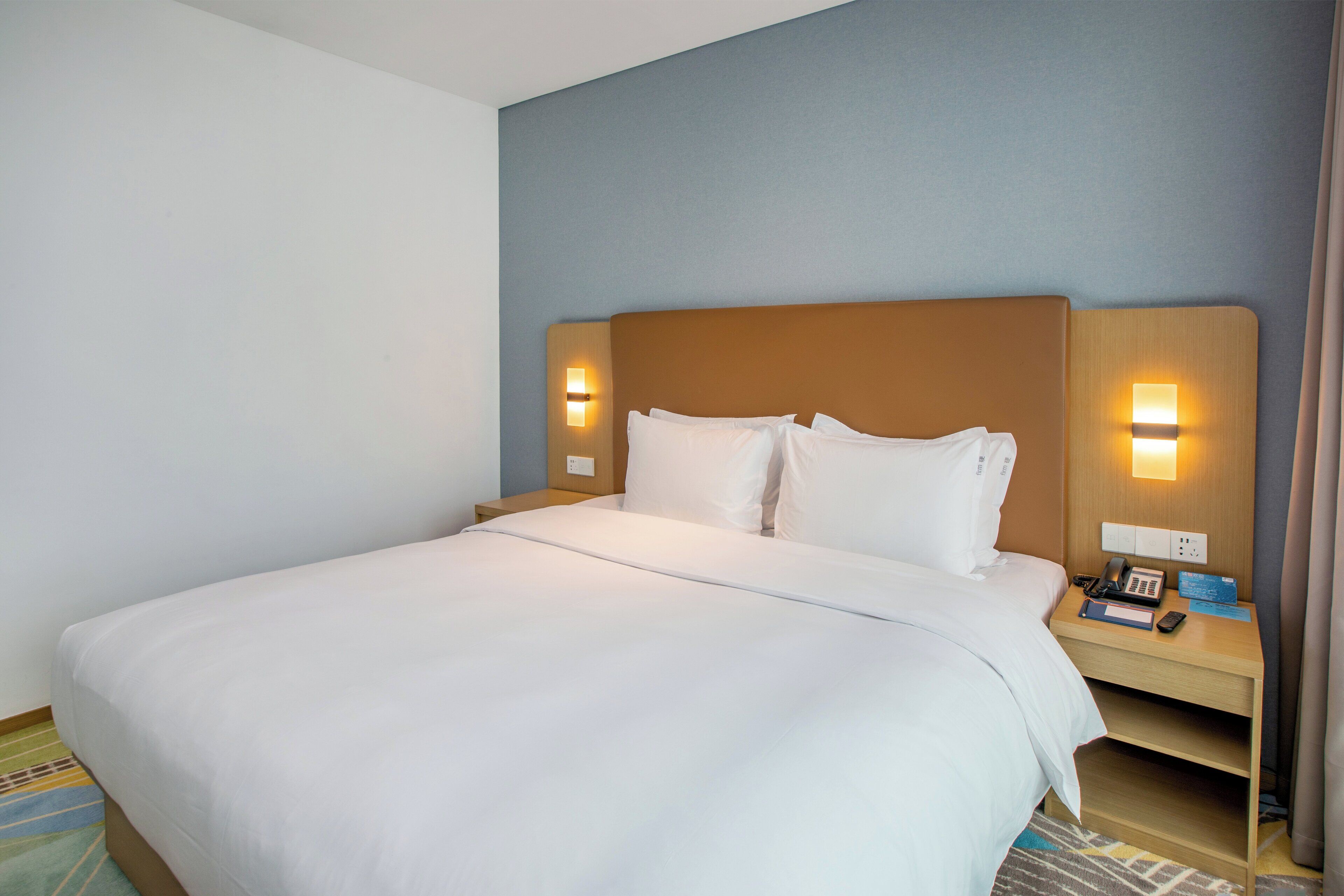 A hotel room with a large bed, two bedside tables, and a nightstand with a phone and a book.