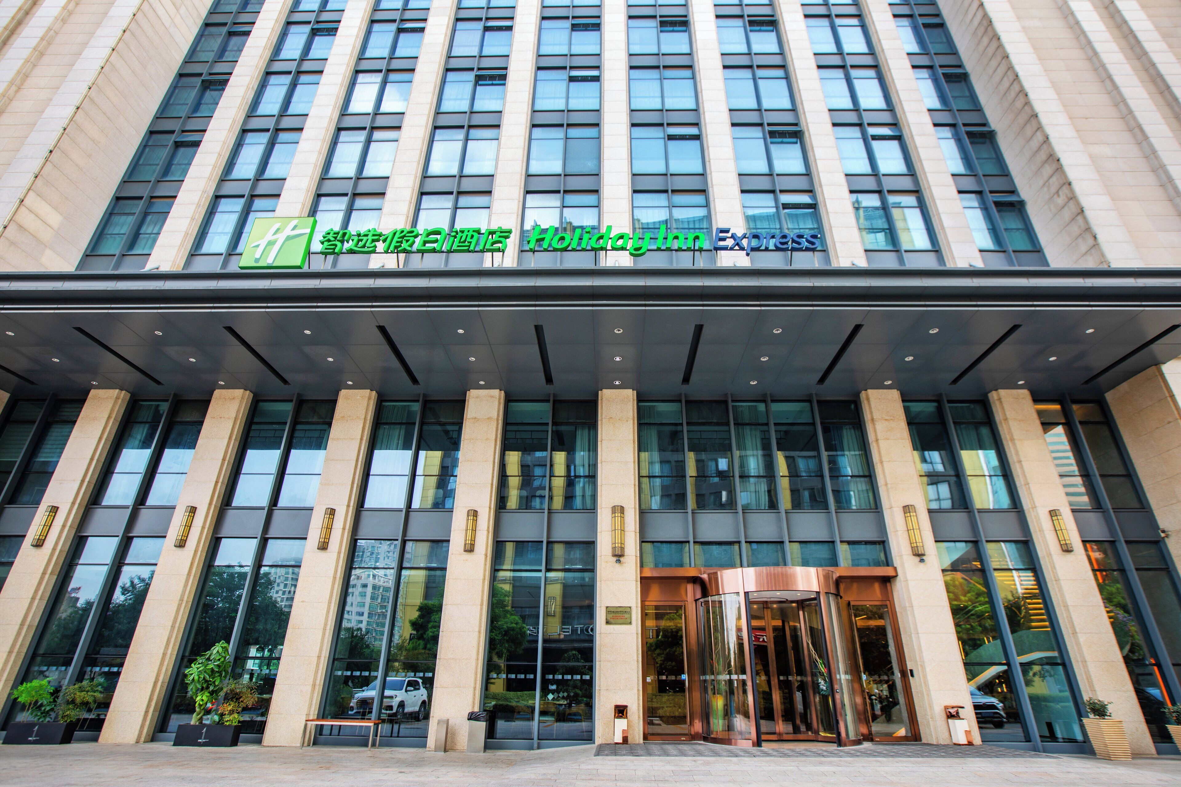 A modern hotel entrance with a glass facade, large windows, and a prominent sign for Holiday Inn Express.
