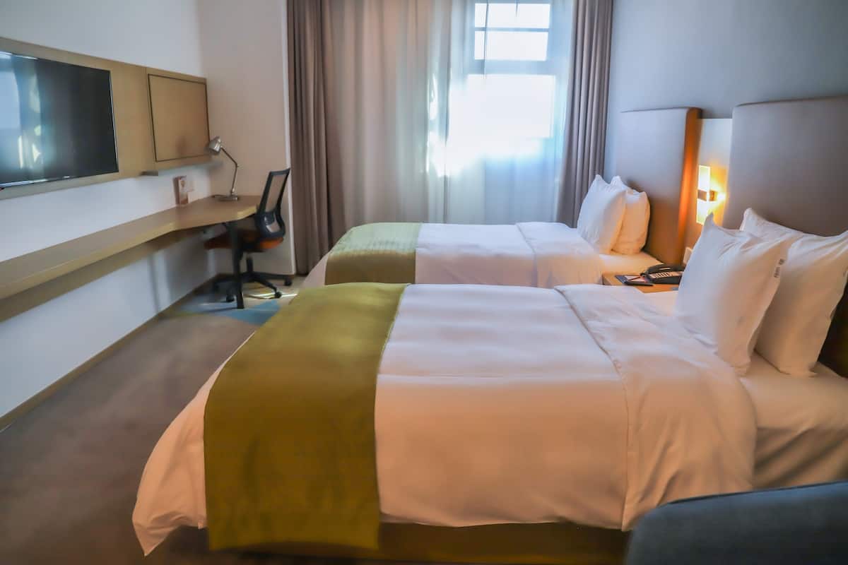 A hotel room with two beds, a desk, a chair, a TV, and a window with curtains.
