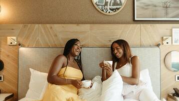 A hotel room with a bed, two pillows, a bedside table, and a wall with framed pictures.