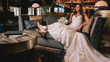 Una persona con vestido de novia sentada en un sofá en un interior moderno, con una barra y estanterías al fondo.