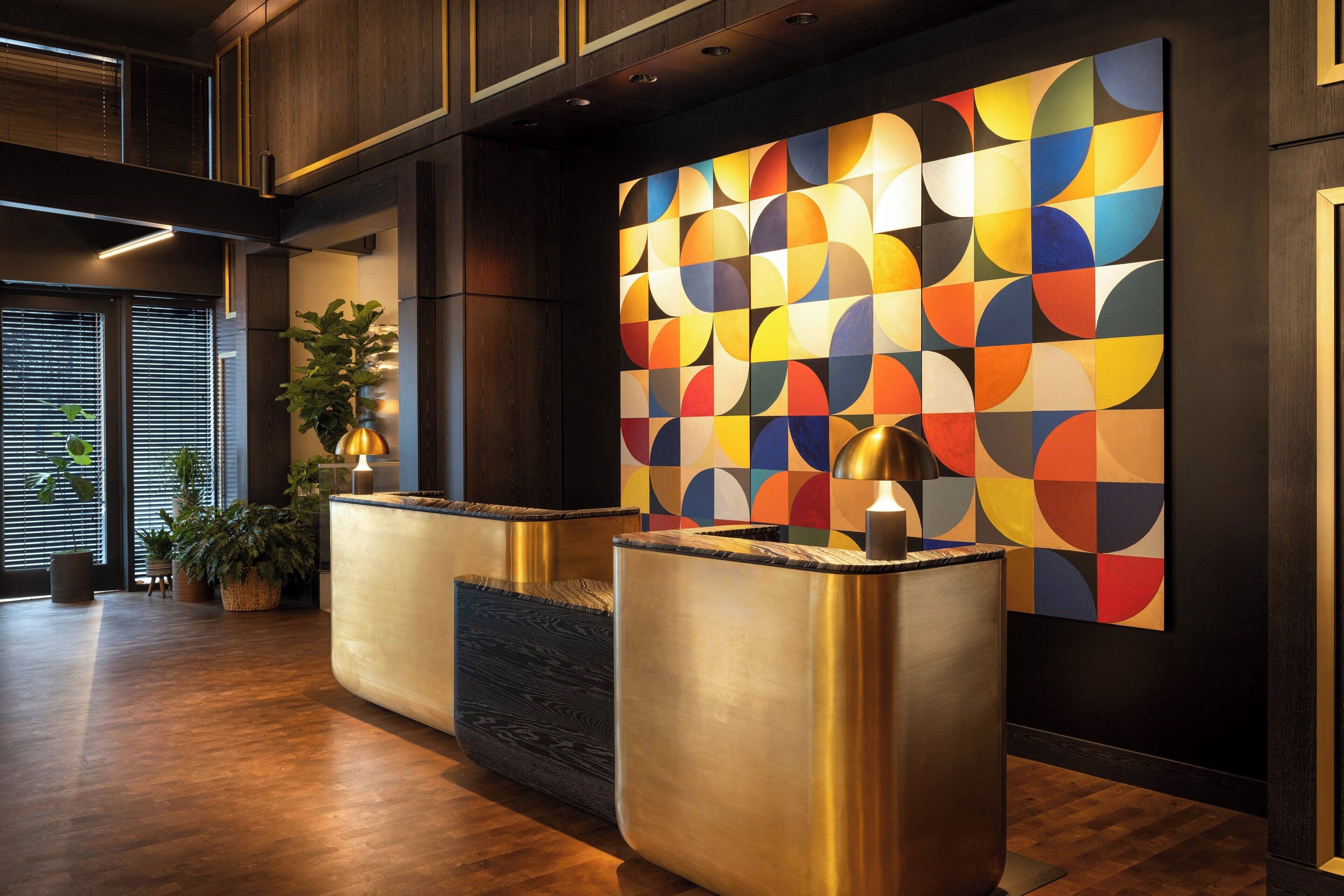 A reception area with a modern design, featuring a colorful geometric wall art, a reception desk, and a potted plant.