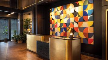 A reception area with a modern design, featuring a colorful geometric wall art, a reception desk, and a potted plant.