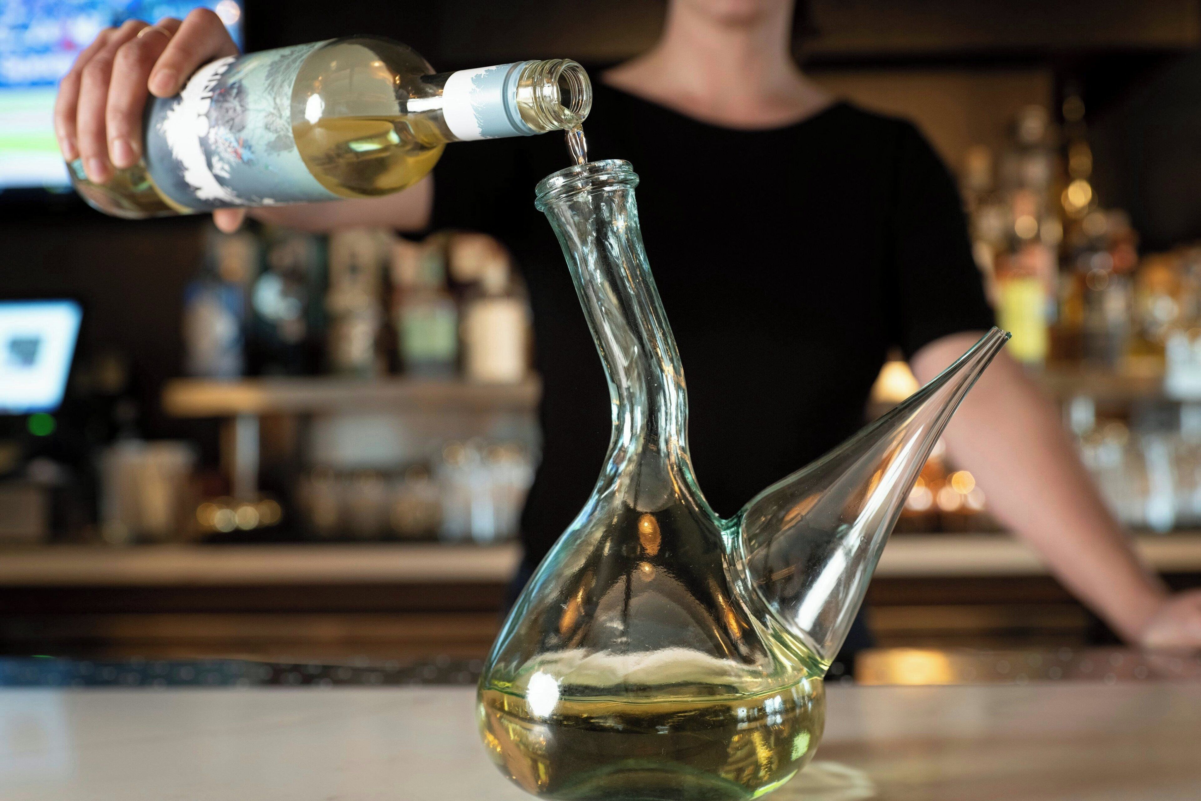 A person pouring a liquid from a bottle into a clear glass container.