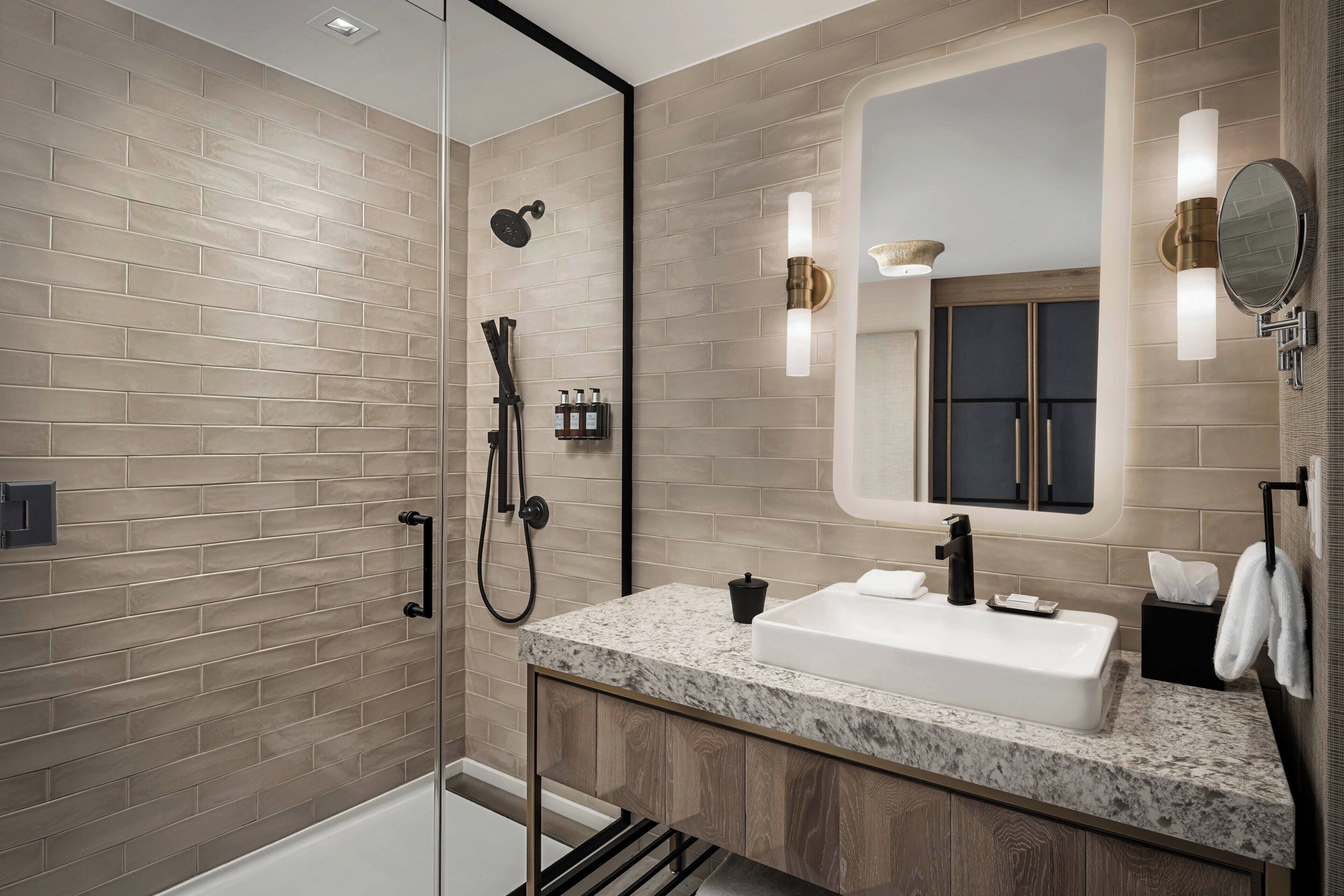 A modern bathroom with a glass shower enclosure, a marble sink, and a large mirror with wall sconces.
