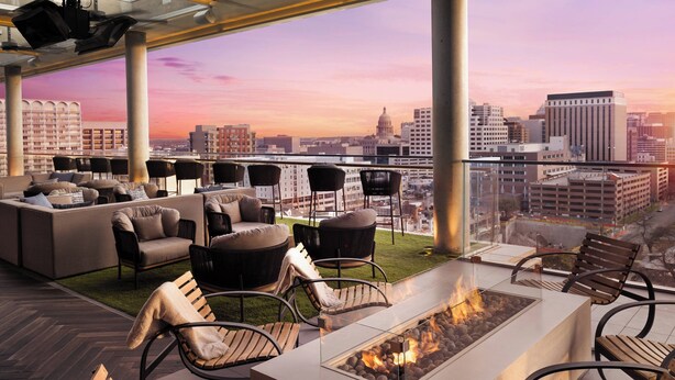 A rooftop lounge with outdoor seating, a fire feature, and a city view at sunset. - The Otis Hotel Austin, Autograph Collection (Austin)