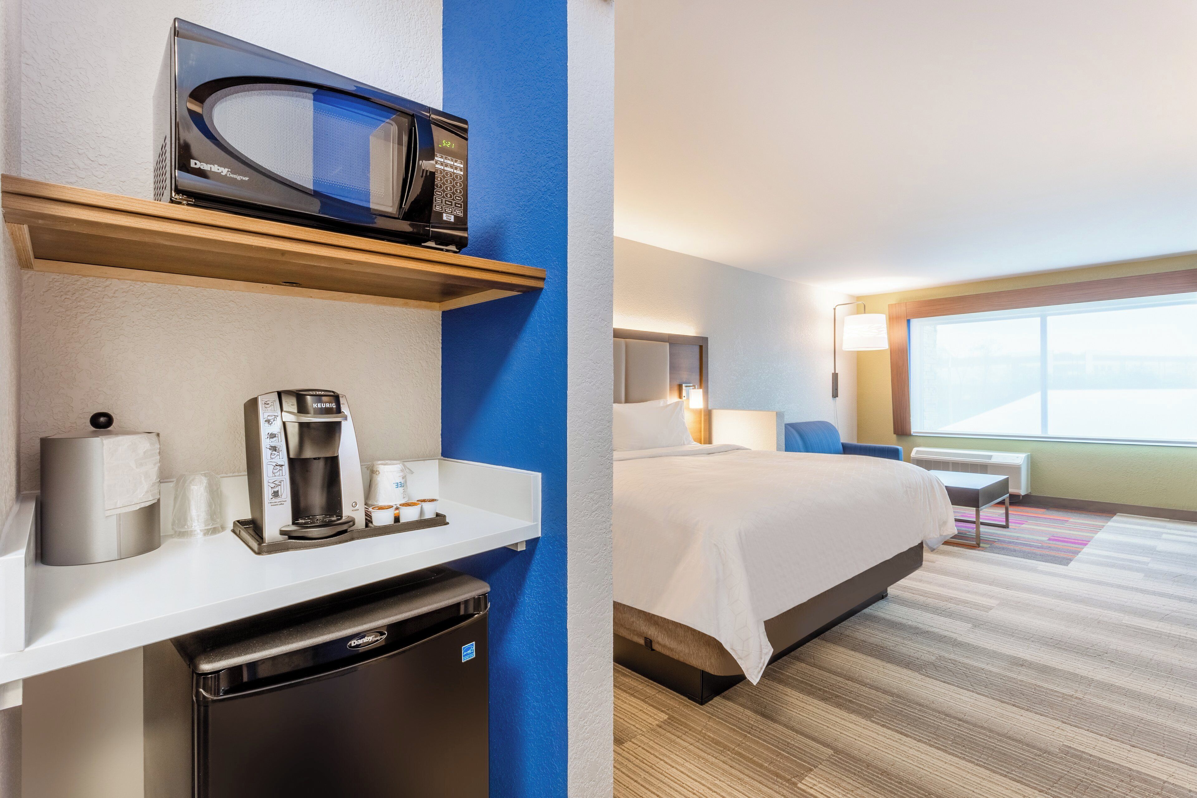 A hotel room with a kitchenette, a bed, a window with a view, and a bedside table.