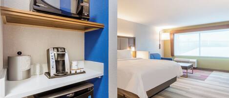 A hotel room with a kitchenette, a bed, a window with a view, and a bedside table.