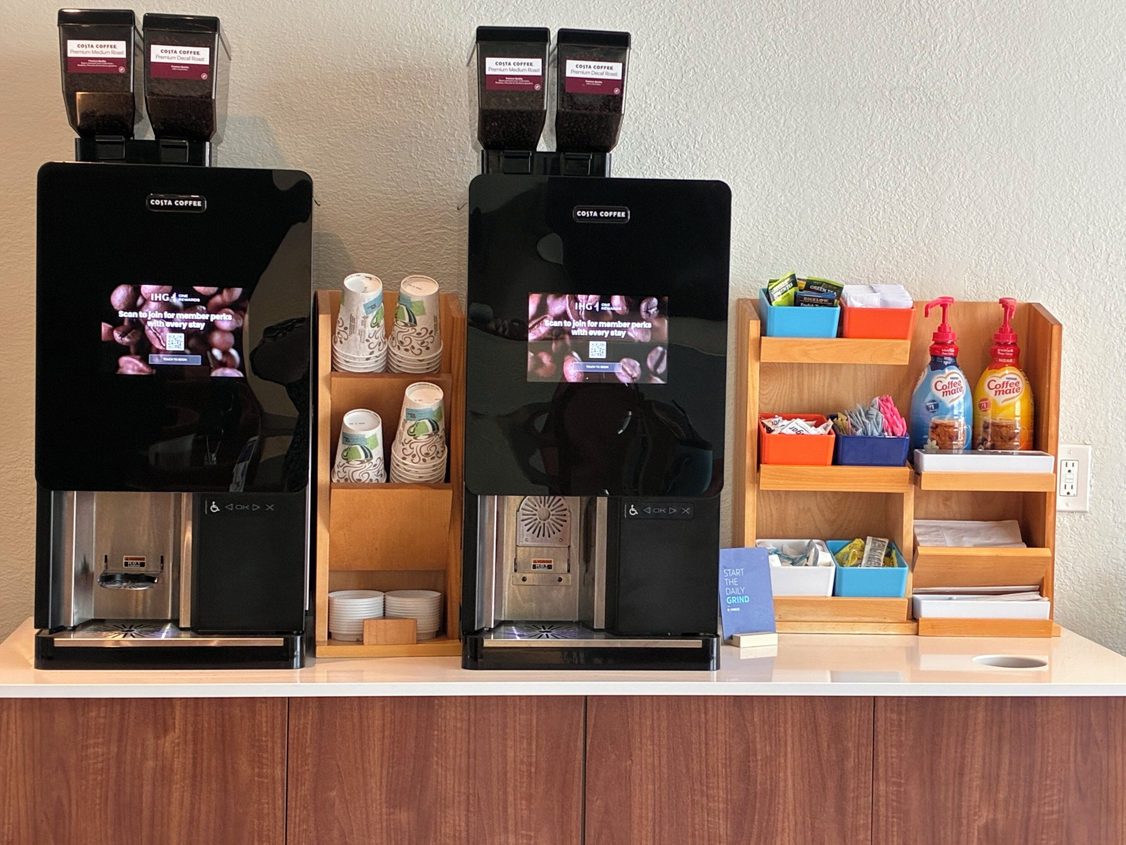 Deux machines à café, une pile de gobelets en papier et une étagère remplie d’articles liés au café.