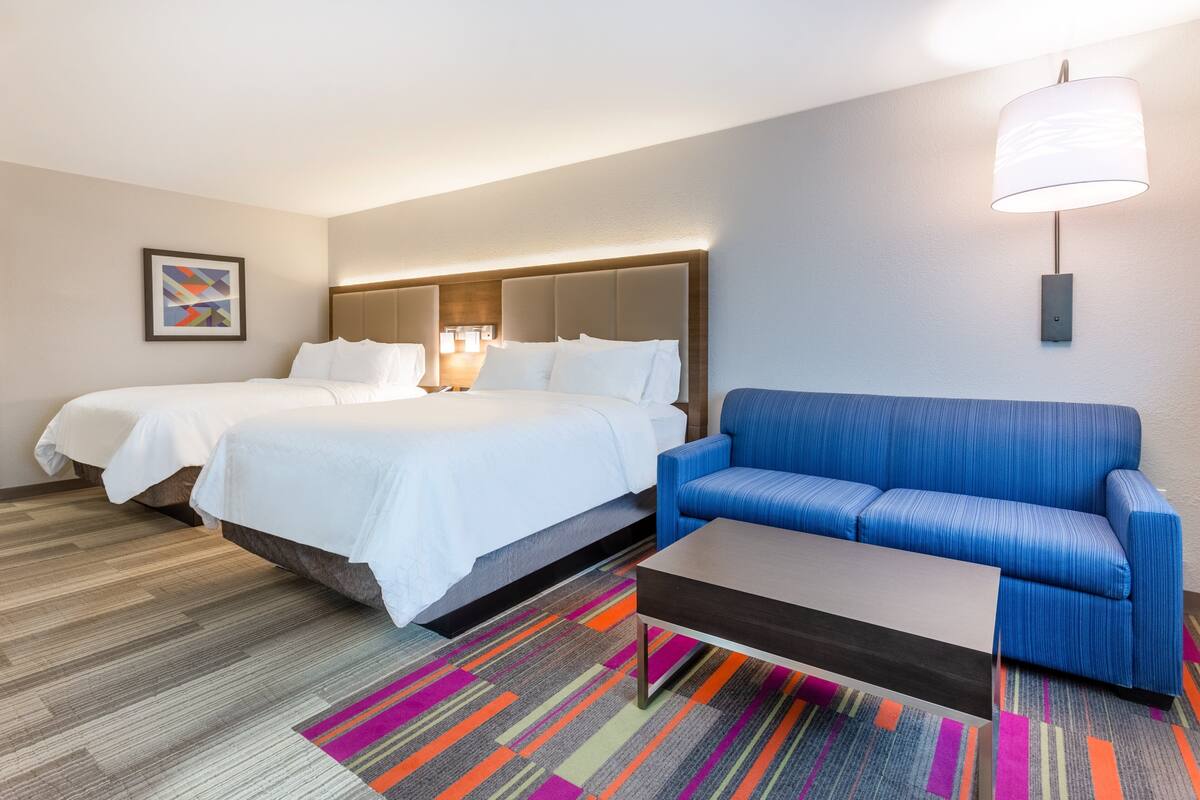 A hotel room with two beds, a blue sofa, a coffee table, and a colorful rug.