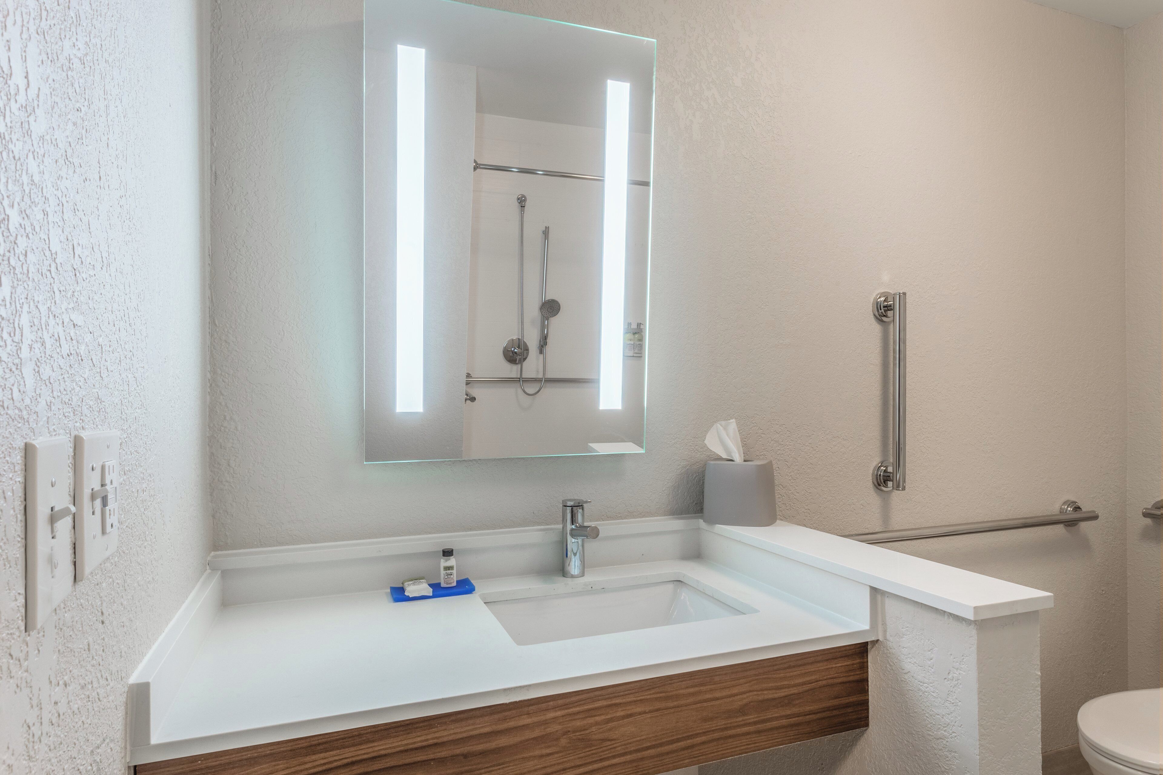 Un bany amb un lavabo blanc, un mirall, una barra de tovalloles i un vàter.