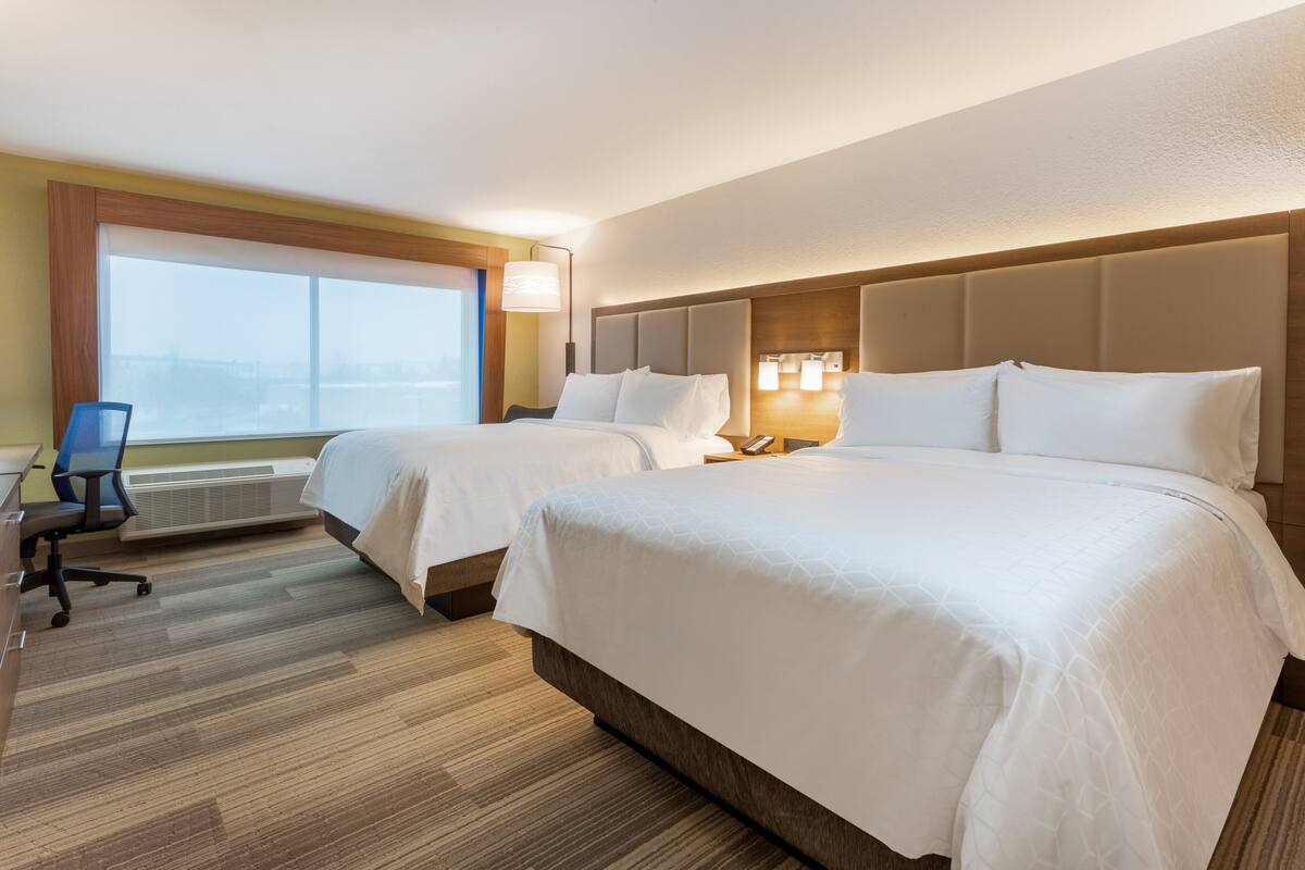 A hotel room with two beds, a desk, and a chair.
