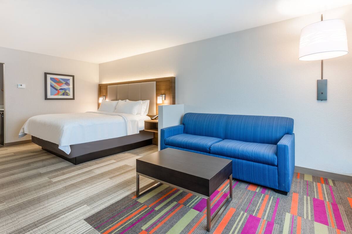 A hotel room with a bed, a sofa, a coffee table, and a lamp.