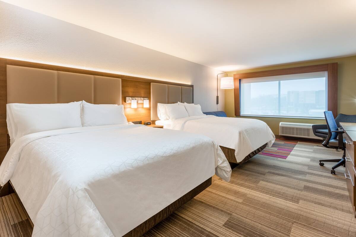 A hotel room with two beds, a desk, and a large window.